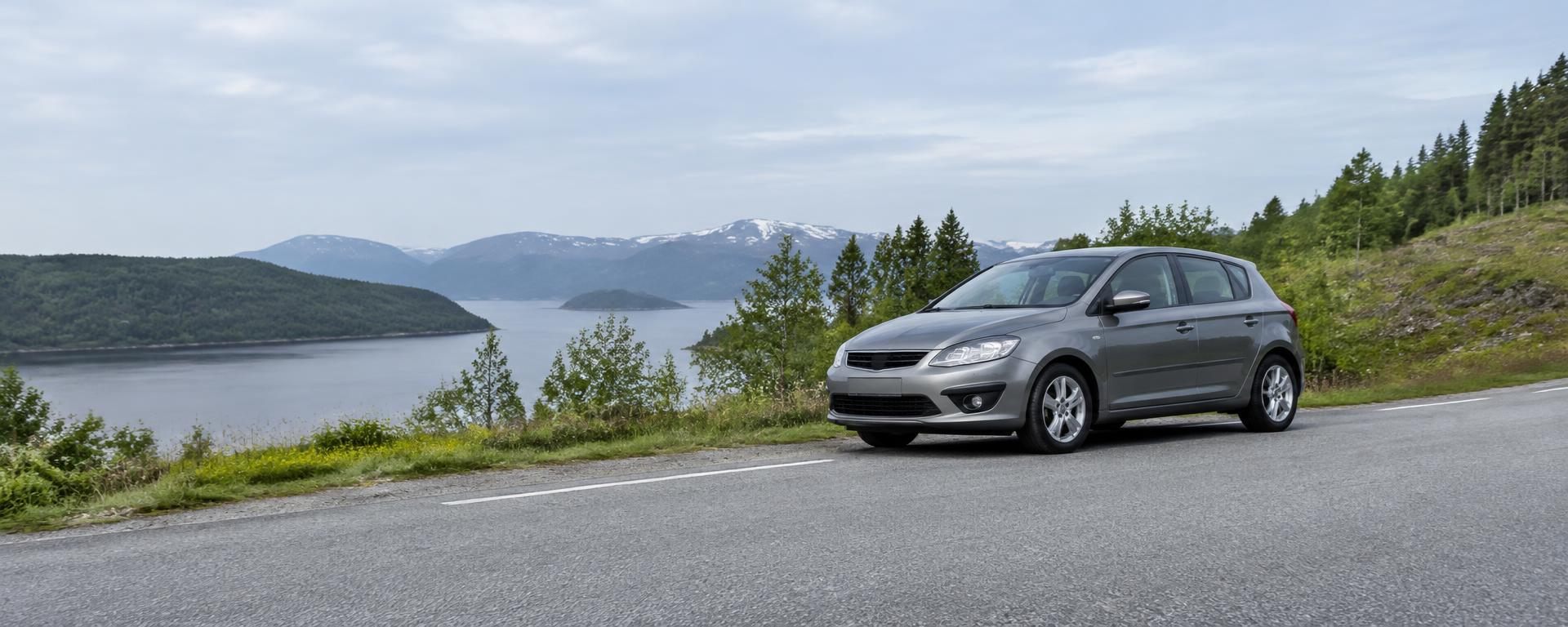 Grå bruktbil parkert ved en rolig norsk vei med fjord i bakgrunnen
